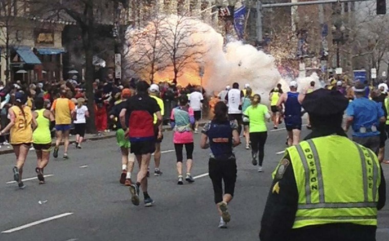 Image: Runners continue to run towards the finish line as an explosion erupts at the finish line of the Boston Marathon